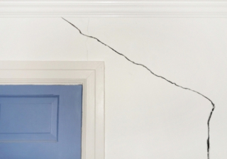 crack in white wall over blue door