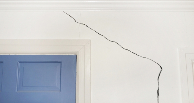 crack in white wall over blue door